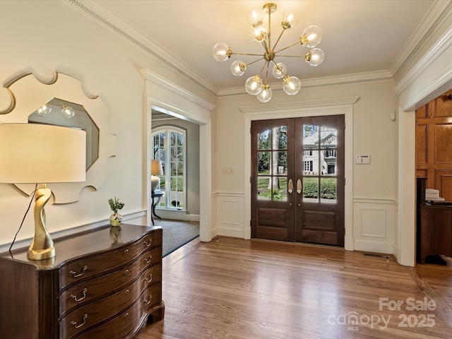 foyer entrance featuring french doors, crown molding, a decorative wall, wood finished floors, and a chandelier