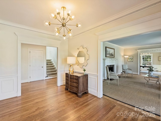 hall featuring a notable chandelier, stairway, wainscoting, light wood-type flooring, and crown molding