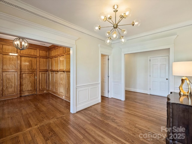 unfurnished dining area with a chandelier, ornamental molding, dark wood-style flooring, and a wainscoted wall