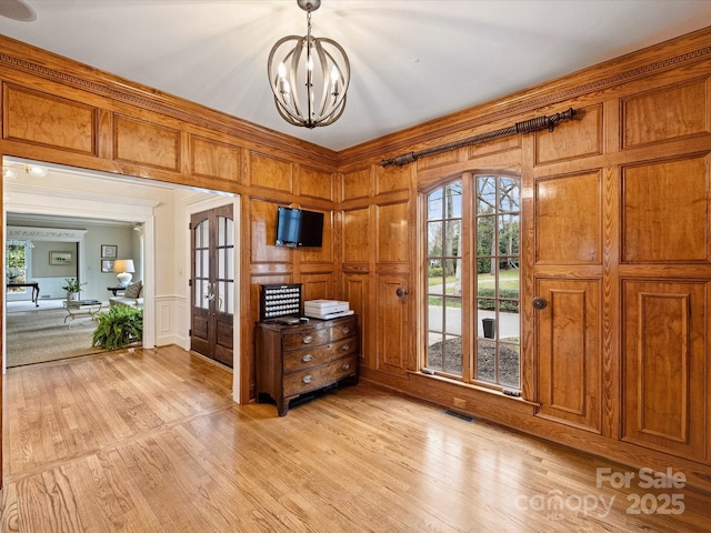 interior space featuring a chandelier, light wood-style floors, visible vents, and a decorative wall