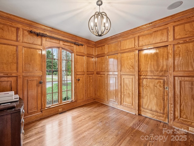 interior space with light wood-style floors, a chandelier, visible vents, and wooden walls