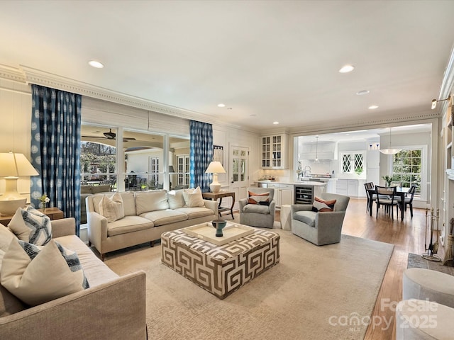 living room featuring light wood-style floors, beverage cooler, ornamental molding, and recessed lighting