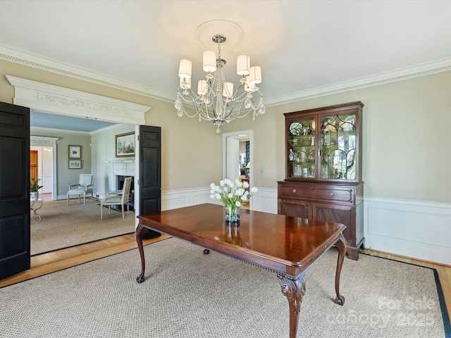 dining space with a chandelier, a wainscoted wall, a fireplace, wood finished floors, and ornamental molding