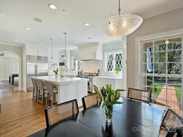 dining area featuring plenty of natural light, arched walkways, crown molding, and light wood finished floors