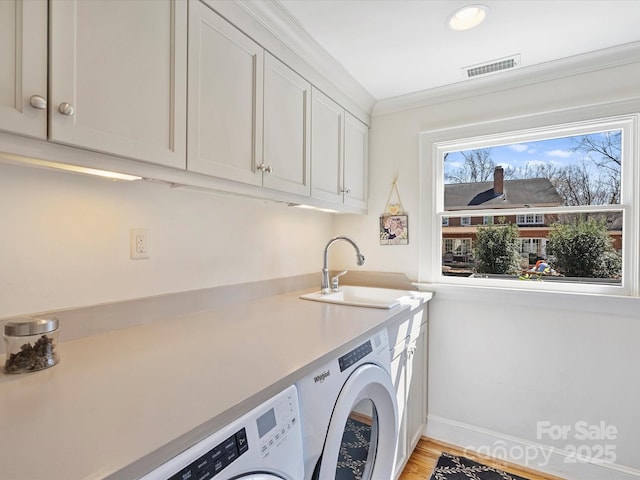 washroom with crown molding, cabinet space, visible vents, washing machine and dryer, and a sink