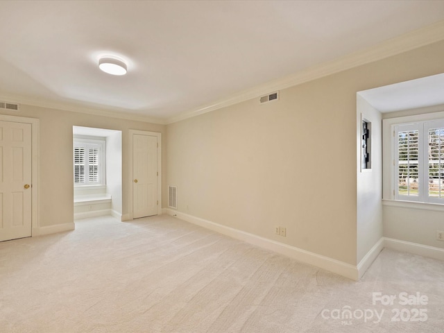 empty room with baseboards, crown molding, visible vents, and light colored carpet