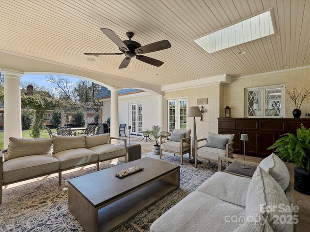 living area featuring decorative columns, arched walkways, a ceiling fan, wood ceiling, and crown molding