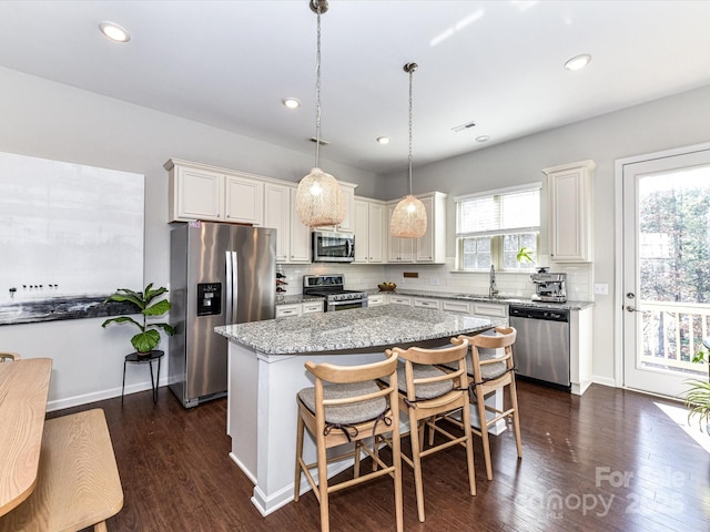 kitchen with light stone counters, dark wood-type flooring, appliances with stainless steel finishes, a center island, and tasteful backsplash