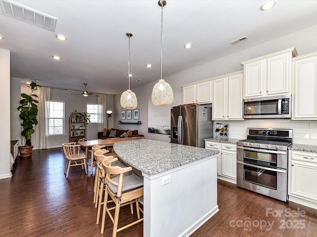 kitchen with appliances with stainless steel finishes, a center island, visible vents, and dark wood-style floors