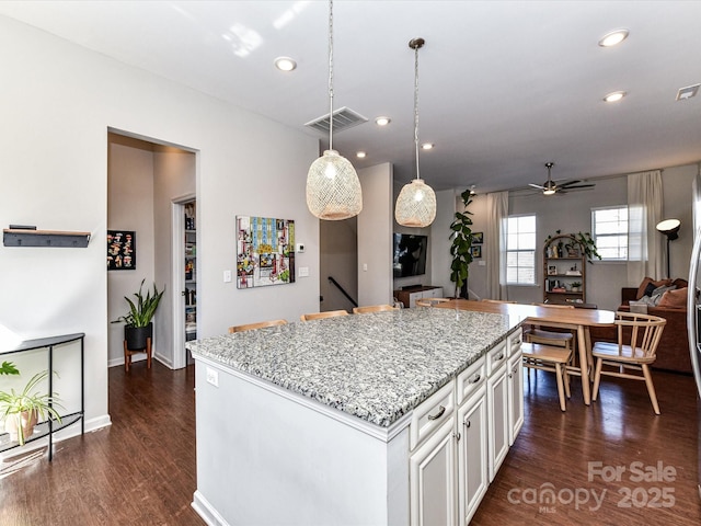 kitchen featuring light stone counters, visible vents, dark wood-type flooring, white cabinets, and a kitchen island