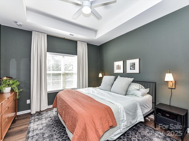 bedroom with baseboards, visible vents, a ceiling fan, wood finished floors, and a tray ceiling