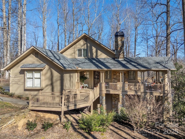 rear view of property featuring a porch, stone siding, roof with shingles, and a chimney