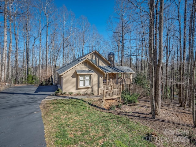 view of front of home with a view of trees, driveway, a chimney, and a front lawn