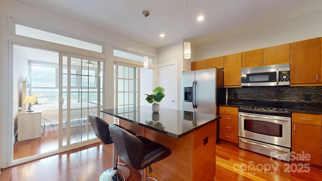 kitchen featuring tasteful backsplash, brown cabinetry, wood finished floors, a center island, and stainless steel appliances