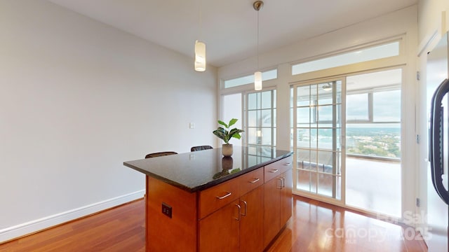 kitchen with light wood finished floors, hanging light fixtures, a kitchen island, dark stone countertops, and baseboards