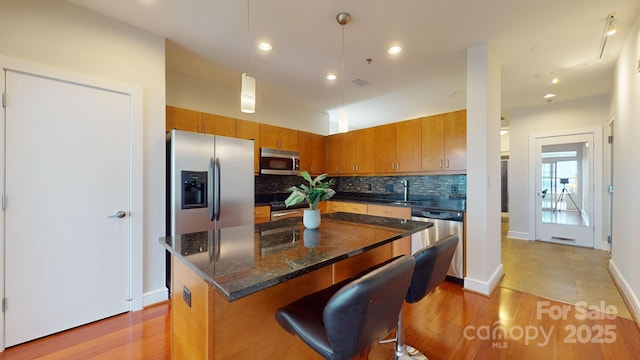 kitchen featuring appliances with stainless steel finishes, brown cabinetry, backsplash, and light wood-style flooring