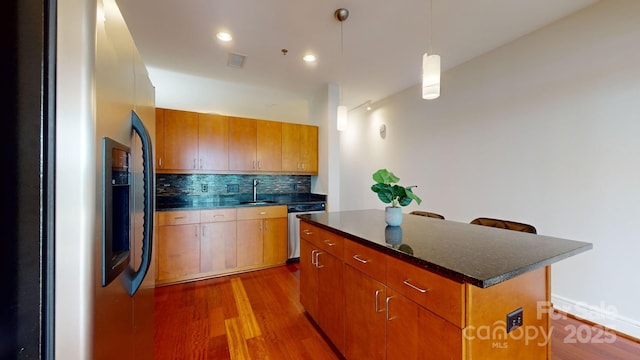 kitchen featuring tasteful backsplash, dark wood finished floors, a kitchen island, stainless steel appliances, and a sink