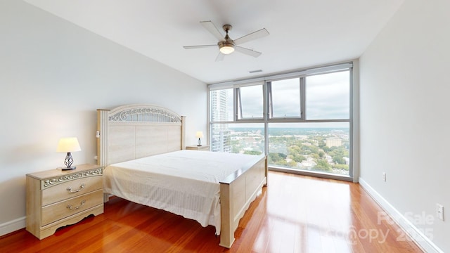 bedroom featuring ceiling fan, wood finished floors, visible vents, baseboards, and floor to ceiling windows