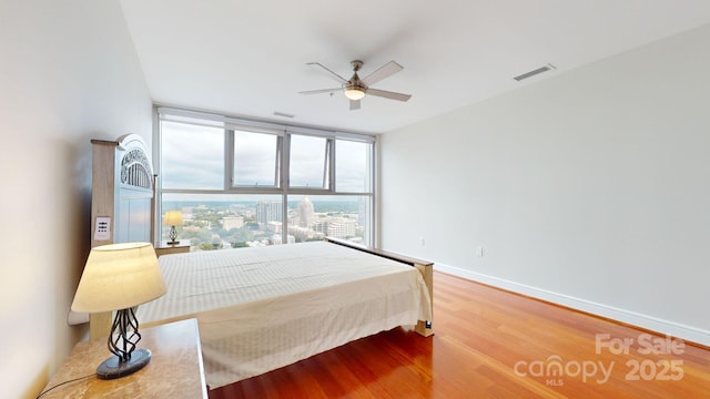 bedroom with baseboards, visible vents, ceiling fan, wood finished floors, and expansive windows