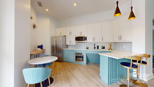 kitchen with light wood finished floors, stainless steel appliances, decorative backsplash, and light countertops