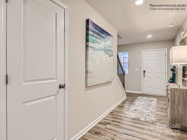 foyer entrance featuring stairway, visible vents, light wood-style flooring, and baseboards