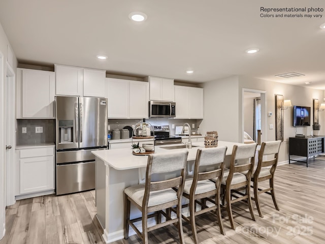 kitchen featuring visible vents, appliances with stainless steel finishes, a sink, light wood-style floors, and backsplash