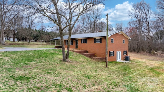 view of front facade featuring brick siding, central AC unit, metal roof, a yard, and driveway