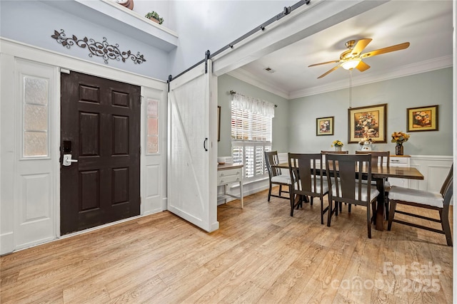 foyer featuring a barn door, visible vents, a ceiling fan, light wood-style flooring, and ornamental molding