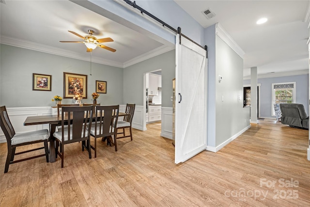 dining space with visible vents, crown molding, light wood-style flooring, and a barn door