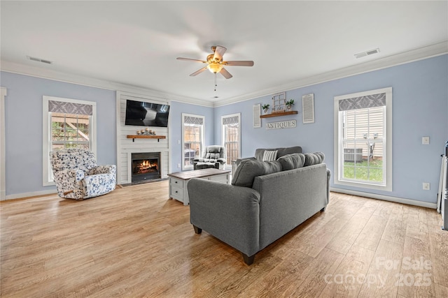 living area featuring light wood-style flooring, visible vents, a wealth of natural light, and ornamental molding