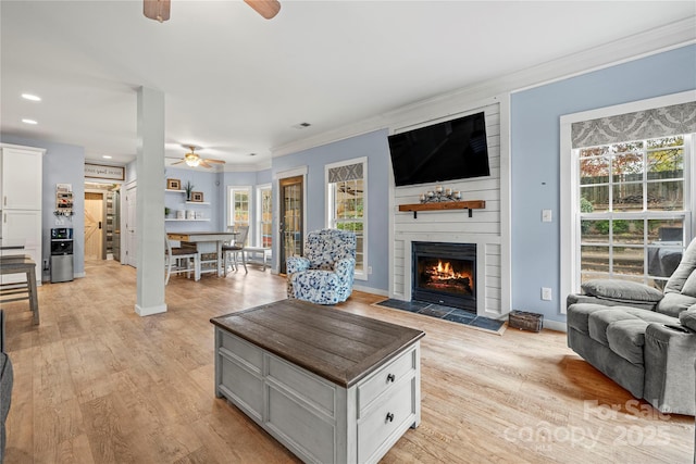 living area featuring ceiling fan, a fireplace, baseboards, ornamental molding, and light wood-type flooring