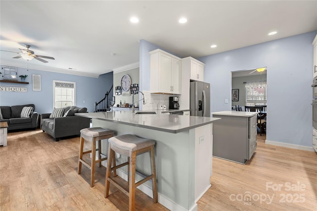 kitchen featuring ceiling fan, a kitchen island, a sink, decorative backsplash, and stainless steel fridge