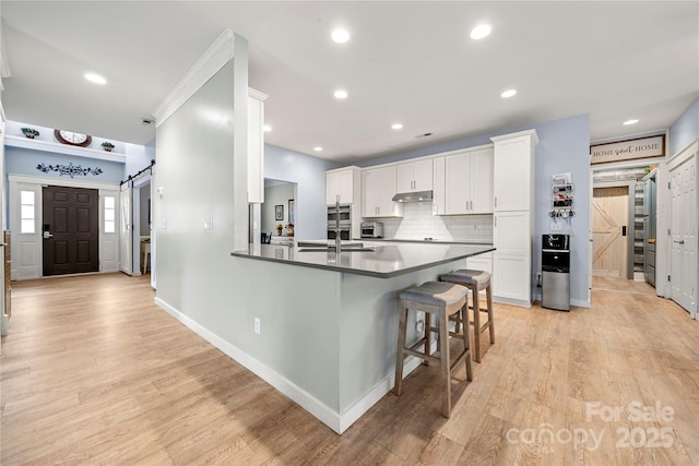 kitchen with light wood finished floors, a barn door, white cabinets, a breakfast bar, and a sink