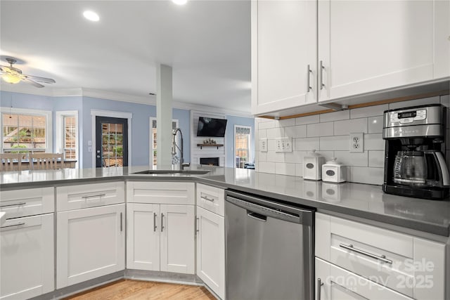 kitchen with a fireplace, a sink, white cabinets, decorative backsplash, and dishwasher