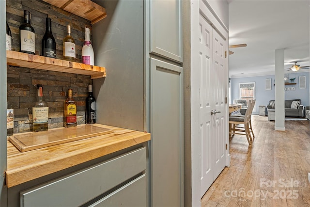 bar with ceiling fan, a dry bar, ornamental molding, and light wood-style floors