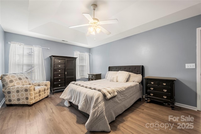 bedroom with visible vents, baseboards, a raised ceiling, ceiling fan, and wood finished floors