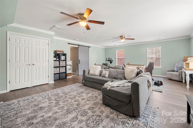 living room with a barn door, visible vents, wood finished floors, and ornamental molding