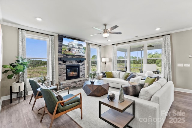 living area with a wealth of natural light, a stone fireplace, baseboards, and wood finished floors