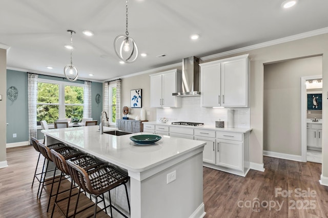 kitchen with a breakfast bar, tasteful backsplash, a sink, wall chimney range hood, and gas cooktop