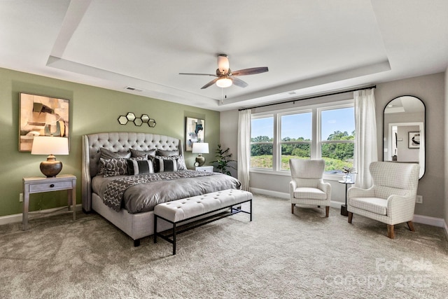 carpeted bedroom with a tray ceiling, a ceiling fan, visible vents, and baseboards