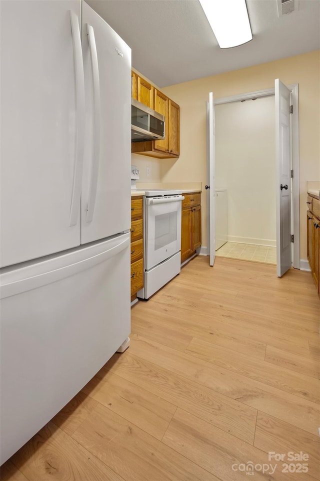 kitchen featuring brown cabinets, white appliances, light countertops, and light wood-type flooring