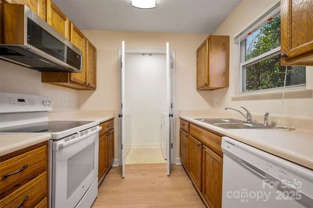 kitchen featuring white appliances, light wood finished floors, a sink, light countertops, and brown cabinets