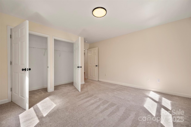 unfurnished bedroom featuring light carpet, two closets, and baseboards