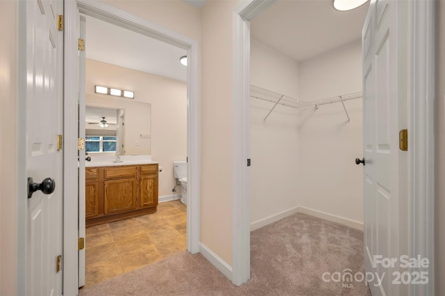 interior space with a walk in closet, toilet, vanity, and baseboards