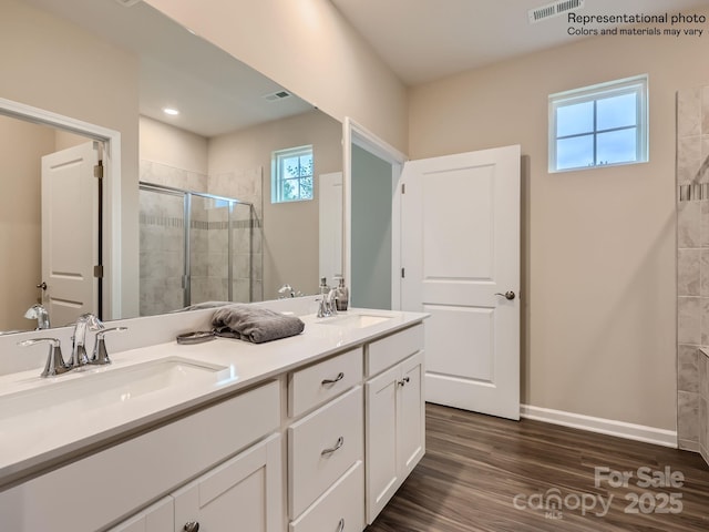 bathroom featuring double vanity, a sink, a shower stall, and wood finished floors