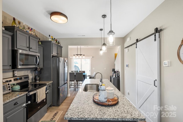 kitchen with stainless steel appliances, decorative backsplash, a barn door, a sink, and an island with sink