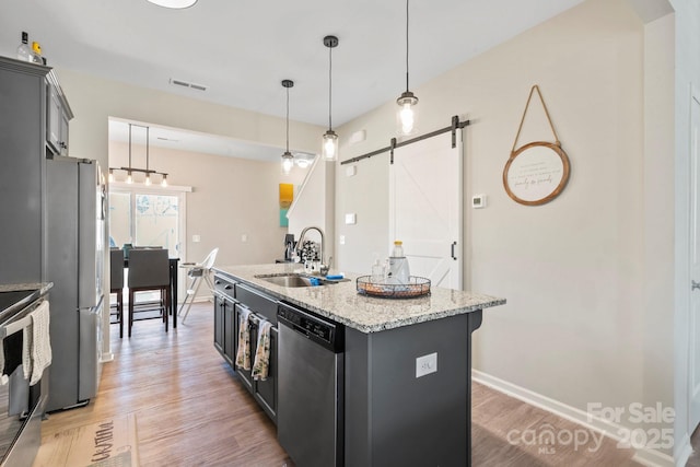 kitchen with a barn door, appliances with stainless steel finishes, light wood-style floors, a kitchen island with sink, and a sink