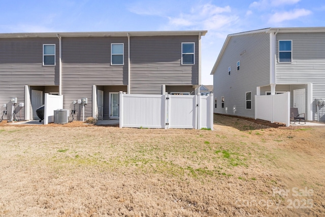 rear view of house with a lawn, cooling unit, a gate, and fence