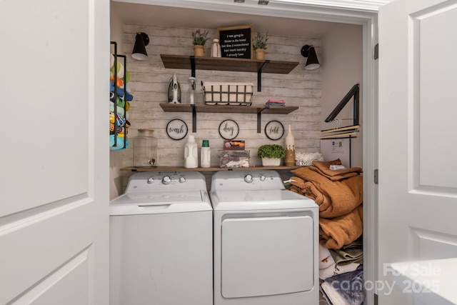 clothes washing area featuring laundry area, wood walls, and washer and clothes dryer