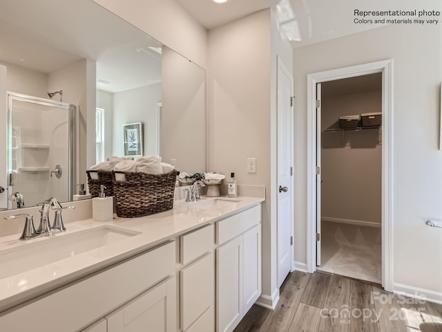 bathroom with a walk in closet, double vanity, a stall shower, a sink, and wood finished floors